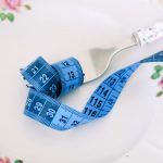 A floral plate with a fork and blue measuring tape symbolizing dieting or healthy eating.