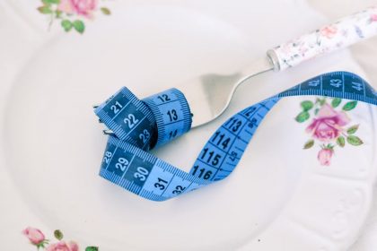 A floral plate with a fork and blue measuring tape symbolizing dieting or healthy eating.